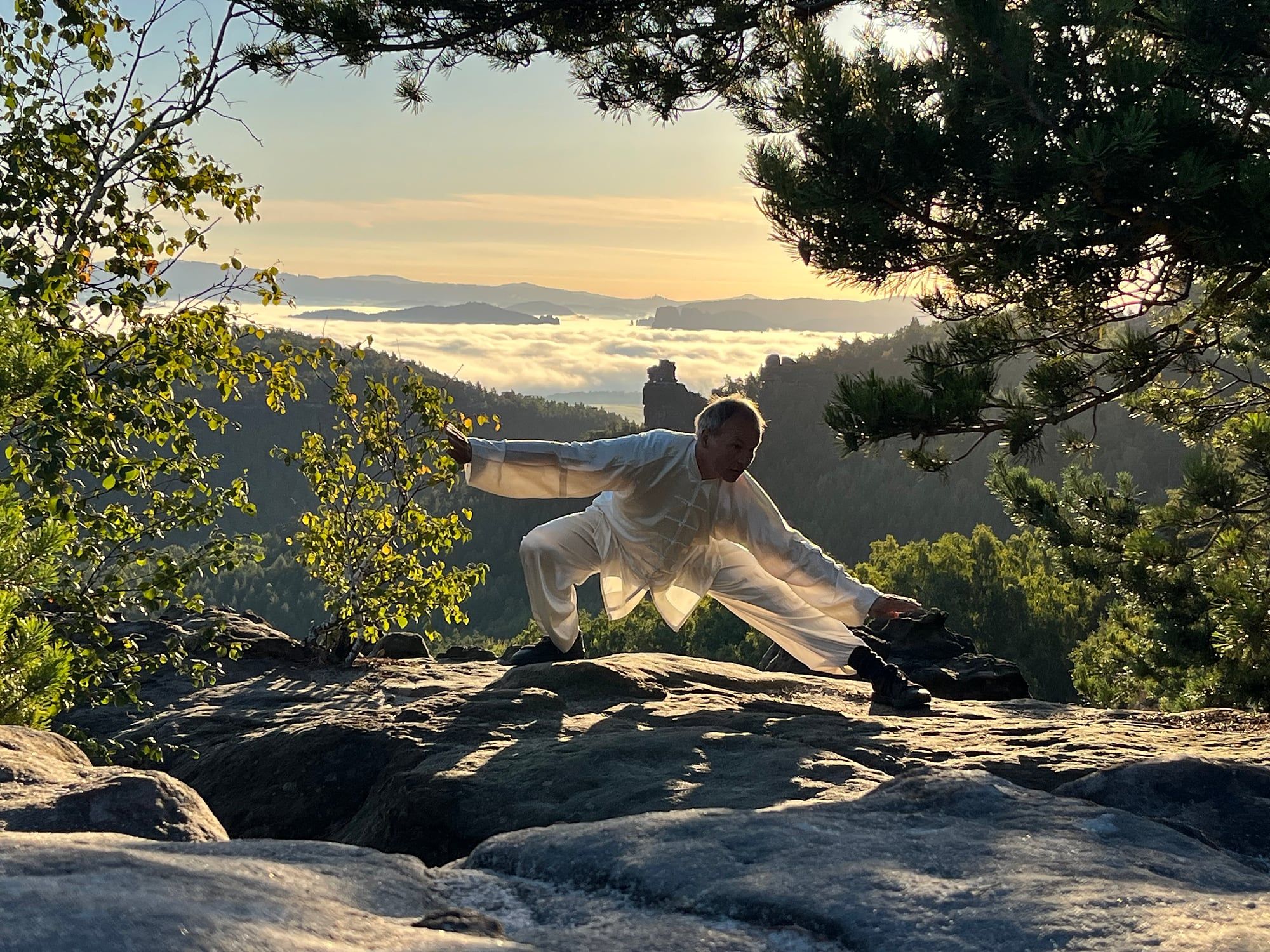 Tai Chi auf einem Felsen im Elbsandsteingebirge, im Gegenlicht Nebel über den Tälern