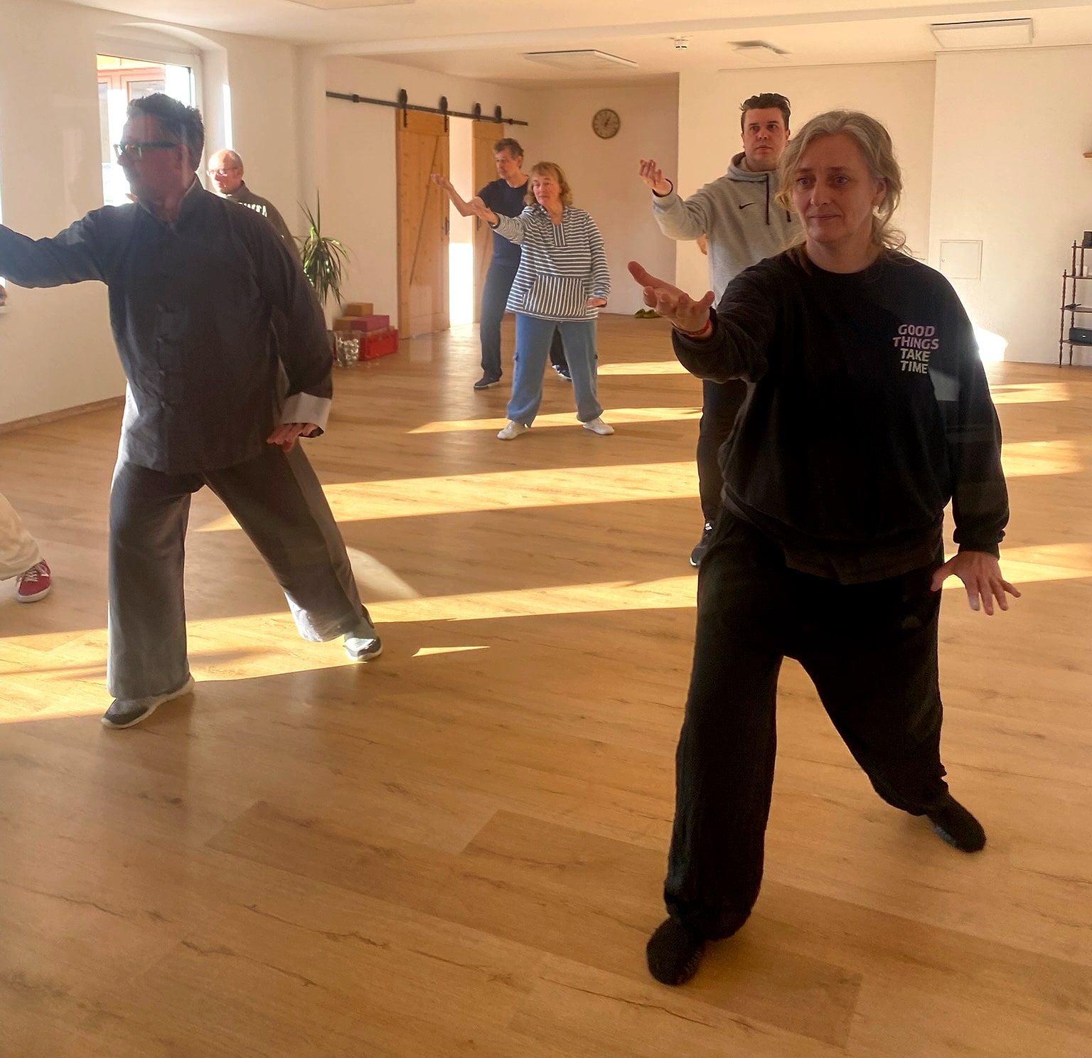 Tai-Chi-Gruppe übt gemeinsam in einem hellen Raum mit Holzboden